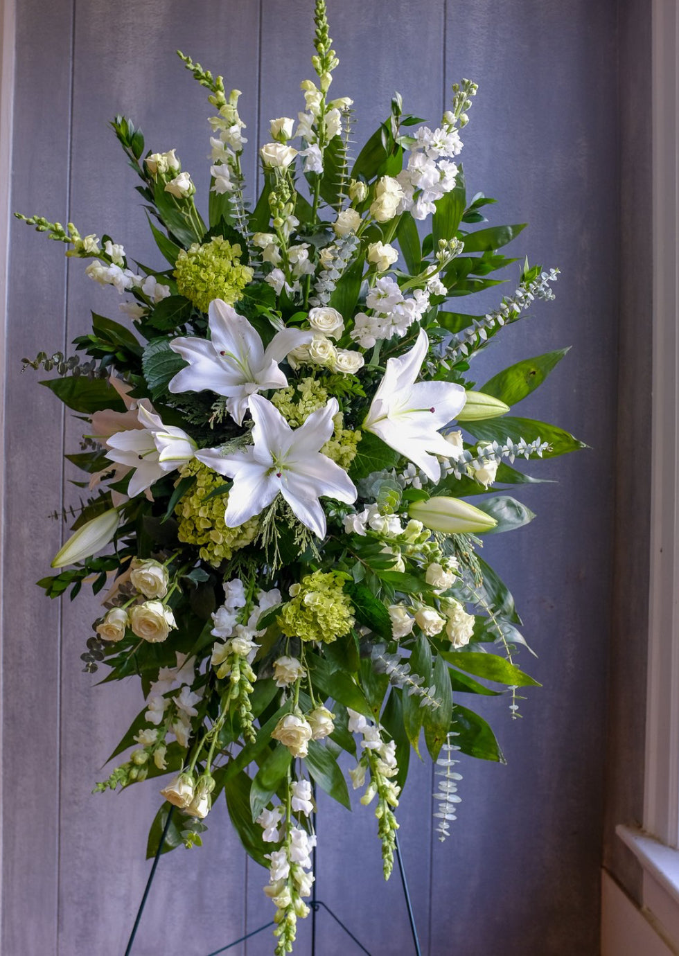 Standing floral spray with white lilies, cream roses, snapdragons, and green hydrangeas symbolizing peace and remembrance – Heavenly Peace Standing Spray by 1800 Blooms Bronx NY