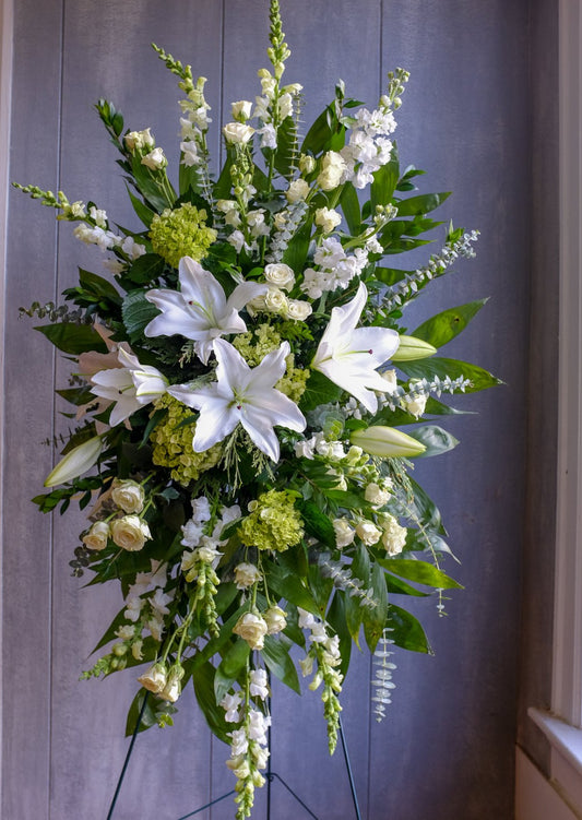Standing floral spray with white lilies, cream roses, snapdragons, and green hydrangeas symbolizing peace and remembrance – Heavenly Peace Standing Spray by 1800 Blooms Bronx NY
